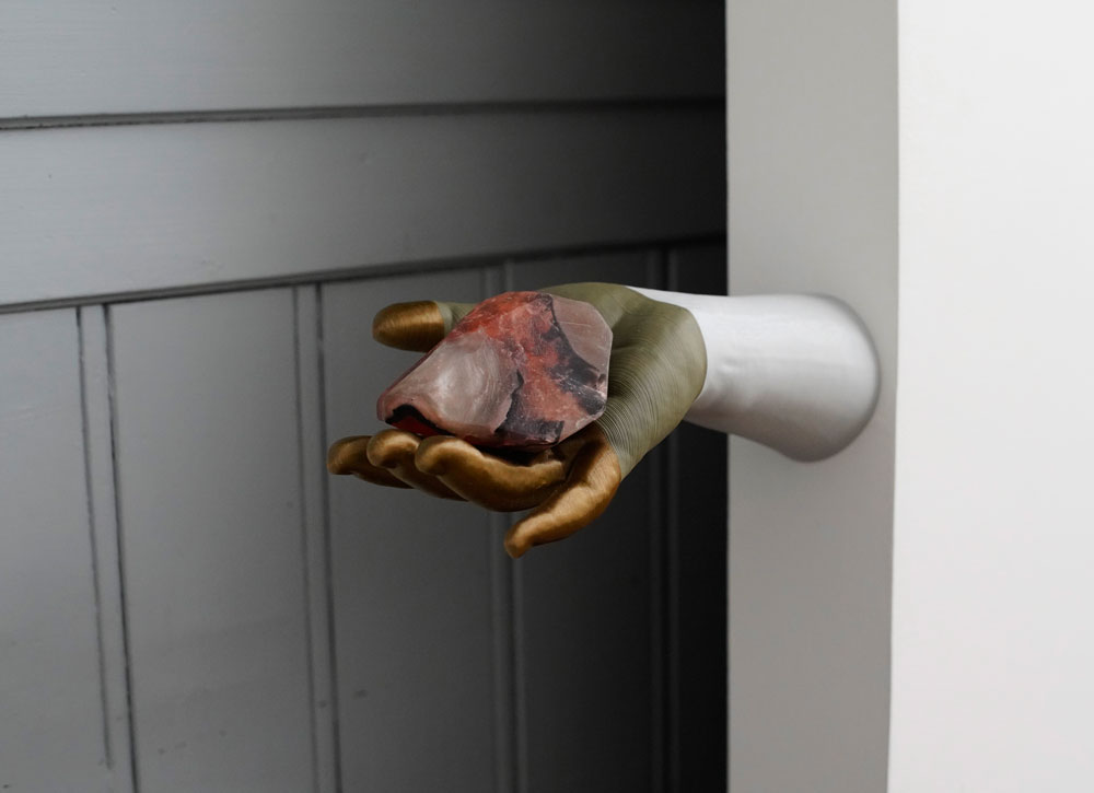 La sculpture de main tenant un caillou de couleur orange-marron.