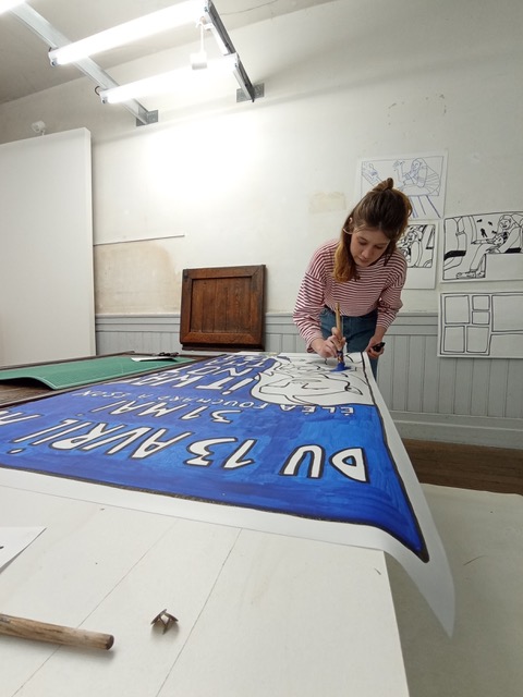 Eléa en train de peindre une affiche dans la salle d'exposition du Quai.
