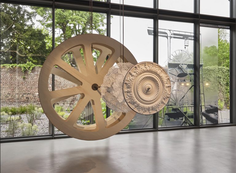 vue d'exposition. Sculpture en céramique et bois figurant des roues de diverses tailles.