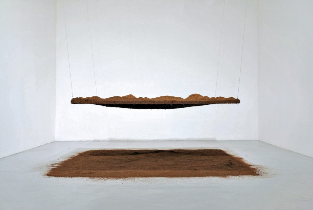 photo d'une sculpture en terre. un carré de terre au sol, un carré de terre en suspention à un mètre du sol.