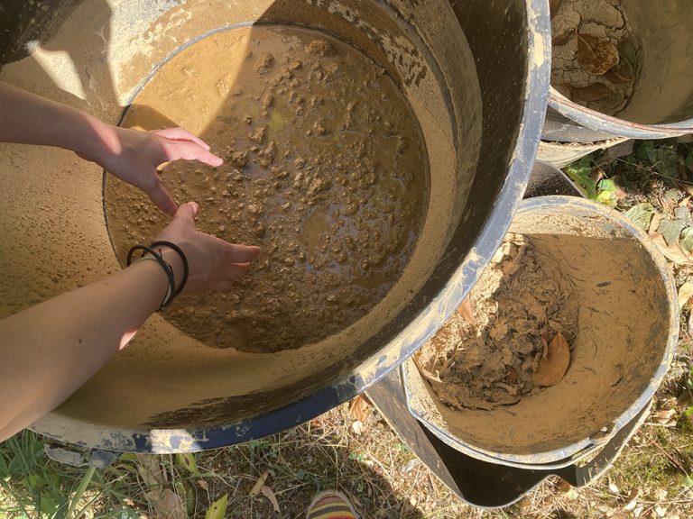 Des mains qui se longent dans une grand poubelle pleine d'argile
