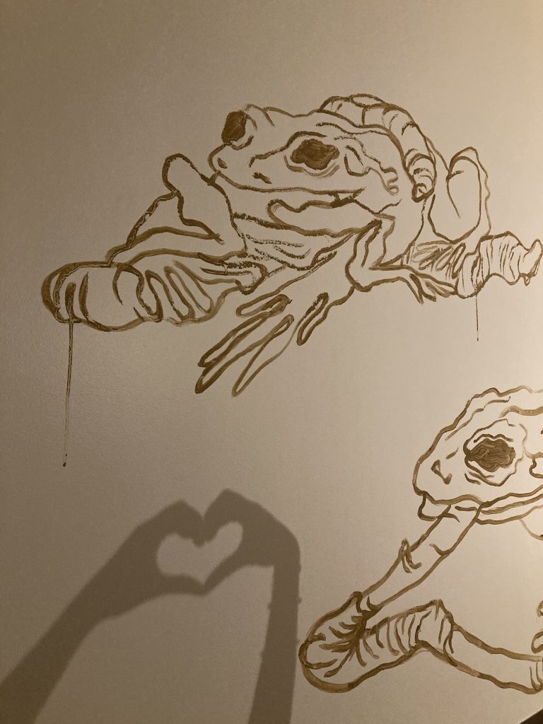 Deux grenouilles dessinées, sur un mur, avec du jus de terre. en dessous, un cœur fait en ombres chinoises avec des mains